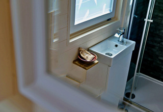 Compact bathroom in 'Marared' Gypsy Hut featuring a small sink, window, and shower in the United Kingdom.