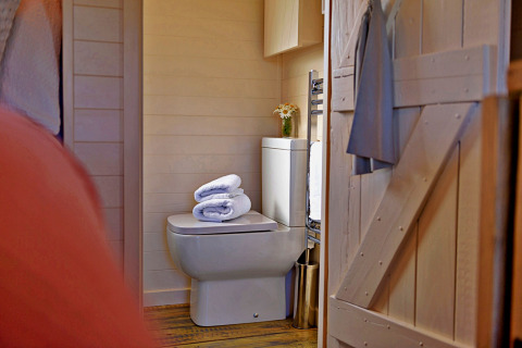 Cozy bathroom inside the 'Marared' Gypsy Hut tiny house in the UK, featuring toilet, towels, and flowers.