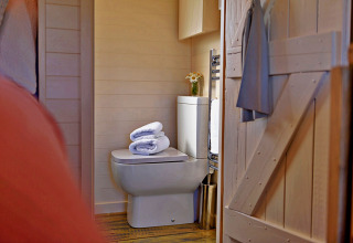 Cozy bathroom inside the 'Marared' Gypsy Hut tiny house in the UK, featuring toilet, towels, and flowers.