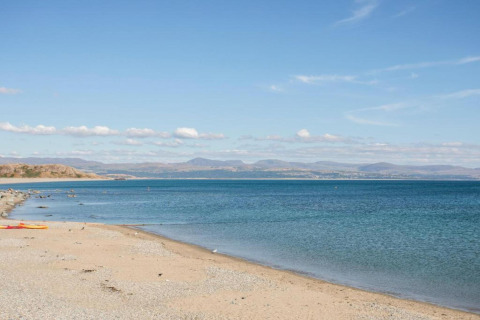 Vue sur la plage et la mer depuis un hébergement glamping, avec montagnes et ciel bleu en arrière-plan.