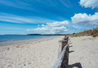 Belle plage de sable calme avec dunes et barrière en bois, parfaite pour un séjour glamping paisible.
