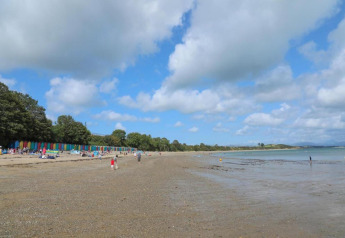 Strand mit bunten Strandhütten und Menschen beim Glamping, Bäumen und bewölktem Sommerhimmel am Meer.