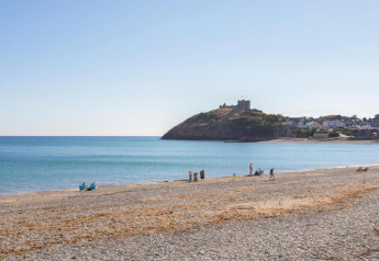 Strand mit wenigen Menschen, ruhigem blauen Meer und einer Burgruine auf dem Hügel bei Glamping.