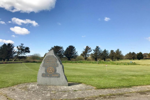 Stone monument by lush green lawn at a glamping site, surrounded by trees and a vibrant blue sky.