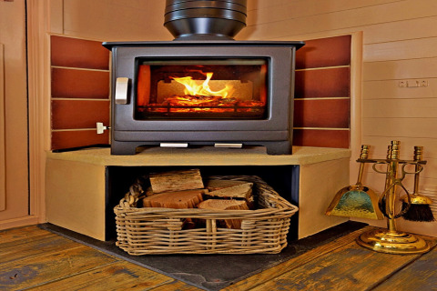 A modern wood-burning stove in a cozy tiny house with a basket of firewood and brass fireplace tools.