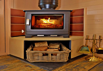Ein moderner Kaminofen in einer gemütlichen Hütte, darunter ein Korb mit Feuerholz auf Holzboden.