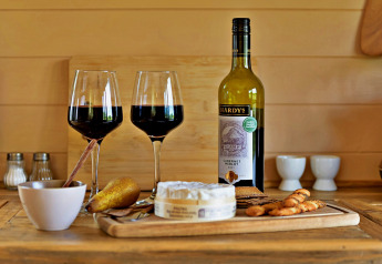 Rotwein, zwei Gläser, Käse, Cracker und Birne auf Holztisch in 'Marared' Gypsy Hut, Tiny House, UK.