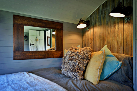 Chambre douillette dans la 'Elen' Gypsy Hut, avec panneaux bois, coussins et miroir, Royaume-Uni.