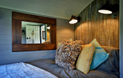 Cozy bedroom inside 'Elen' Gypsy Hut mobile home with rustic wood paneling, pillows, and mirror, UK.