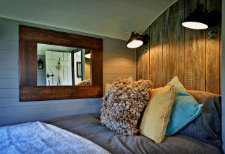 Chambre douillette dans la 'Elen' Gypsy Hut, avec panneaux bois, coussins et miroir, Royaume-Uni.
