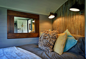 Cozy bedroom inside 'Elen' Gypsy Hut mobile home with rustic wood paneling, pillows, and mirror, UK.