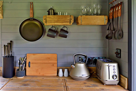 Petite cuisine de mobil-home avec poêle, grille-pain, bouilloire, ustensiles et étagères en bois