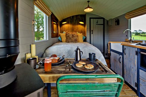 Intérieur de la tiny house 'Elen' Gypsy Hut au Royaume-Uni avec lit douillet, cuisine et table en bois.