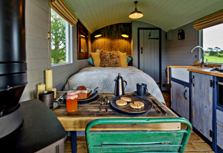Intérieur de la tiny house 'Elen' Gypsy Hut au Royaume-Uni avec lit douillet, cuisine et table en bois.