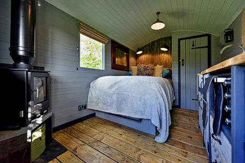 Vue intérieure de « Elen Gypsy Hut » au Royaume-Uni, parquet bois, lit douillet, poêle et coin cuisine.