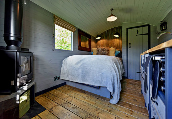 Binnenzicht van de 'Elen' Gypsy Hut in het Verenigd Koninkrijk met houtenvloer, knus bed, kachel en kitchenette.