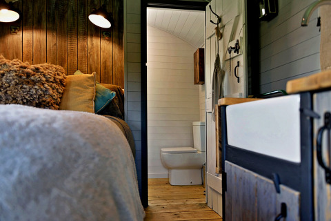 Intérieur du mobil-home 'Elen' Gypsy Hut au Royaume-Uni avec lit douillet et vue sur la salle de bain.