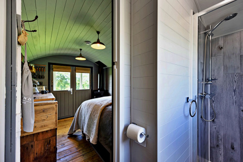 Intérieur du mobil-home 'Elen' Gypsy Hut au Royaume-Uni avec lit, cuisine en bois et douche vitrée.