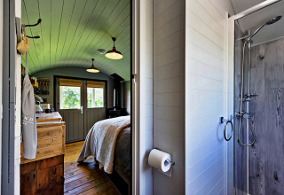 Intérieur du mobil-home 'Elen' Gypsy Hut au Royaume-Uni avec lit, cuisine en bois et douche vitrée.