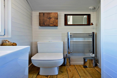 Modern bathroom in 'Elen' Gypsy Hut mobile home featuring wooden floor, toilet, towel heater, and mirror.