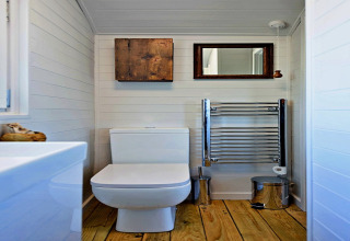 Salle de bain moderne dans la roulotte 'Elen' Gypsy Hut avec sol en bois, toilettes et sèche-serviettes.