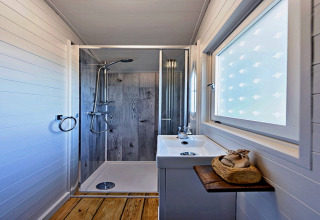 Salle de bain moderne dans la roulotte 'Elen' Gypsy Hut avec douche, lavabo et fenêtre givrée au Royaume-Uni.
