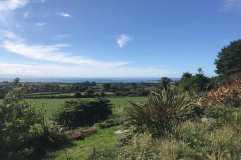 Vue depuis la cabane « Elen » sur des champs verts, des arbres et la mer sous un ciel bleu clair au Royaume-Uni.