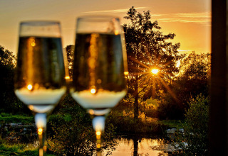 Deux verres de vin pétillant devant un coucher de soleil au bord d’un lac à la roulotte 'Elen' Gypsy Hut au Royaume-Uni.
