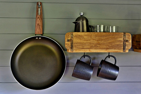 Intérieur de cuisine à la roulotte 'Elen' Gypsy Hut au Royaume-Uni avec poêle, tasses et carafe sur étagère.
