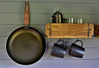 Intérieur de cuisine à la roulotte 'Elen' Gypsy Hut au Royaume-Uni avec poêle, tasses et carafe sur étagère.