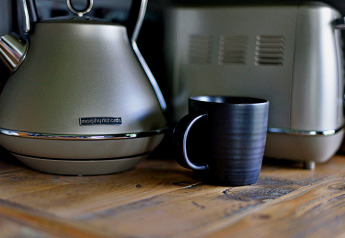Een zwart kopje op een houten tafel naast een Morphy Richards waterkoker in een mobiele woningkeuken.