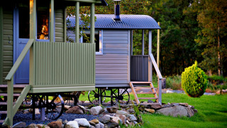 'Elen' Gypsy Hut mobile home with wheels and porch, surrounded by grass, trees, and decorative rocks.