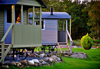 'Elen' Gypsy Hut mobile home with wheels and porch, surrounded by grass, trees, and decorative rocks.