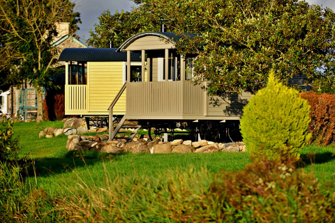 'Elen' Gypsy Hut mobile home in the UK, nestled among trees, shrubs, and a lush green landscape.