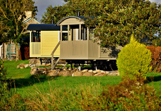 Mobil-home 'Elen' Gypsy Hut au Royaume-Uni, entouré d’arbres, d’arbustes et d’une pelouse verdoyante.