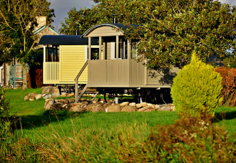 'Elen' Gypsy Hut mobile home in the UK, nestled among trees, shrubs, and a lush green landscape.