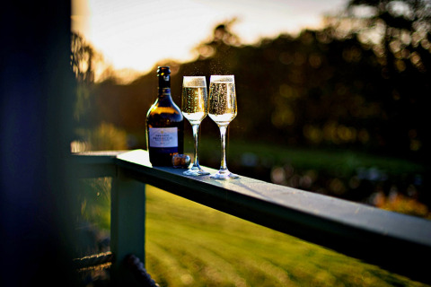 To glas mousserende vin og en flaske på gelænderet ved solnedgang på 'Angharad' Poachers Hut, UK.