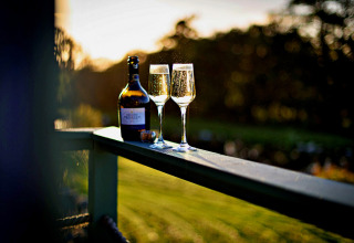 To glas mousserende vin og en flaske på gelænderet ved solnedgang på 'Angharad' Poachers Hut, UK.