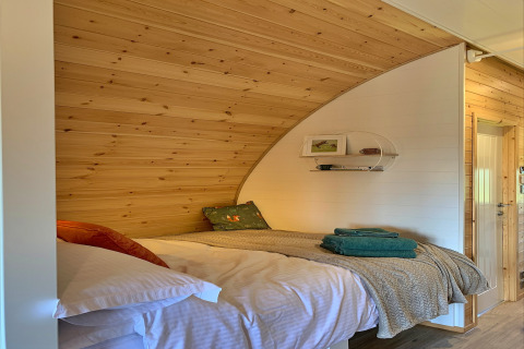 Coin nuit douillet dans la pod Worm Dale au Royaume-Uni, avec bois, lit confortable et serviettes pliées.