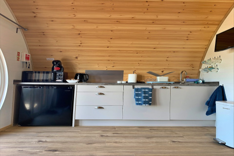 Modern kitchenette in Deep Dale pod, UK, featuring wood ceiling, compact appliances, and utensils.