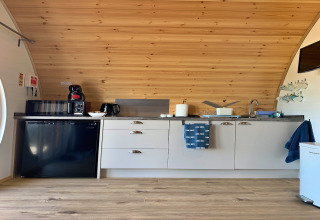 Modern kitchenette in Deep Dale pod, UK, featuring wood ceiling, compact appliances, and utensils.