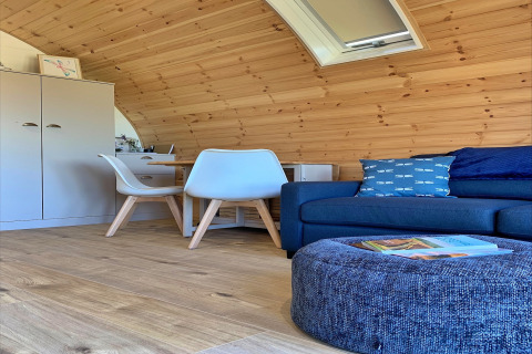 Modern wooden pod interior with sofa, pillows, chairs, and table in Deep Dale, United Kingdom.