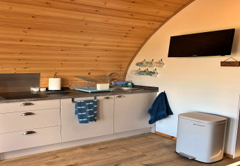 Moderne kitchenette in een houten pod 'Deep Dale' met tv, vuilbak, handdoeken en kopjes aan de muur.