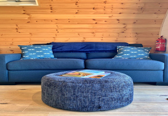 Blauwe sofa met kussens en ronde poef in houten Deep Dale pod, Verenigd Koninkrijk, overdag.