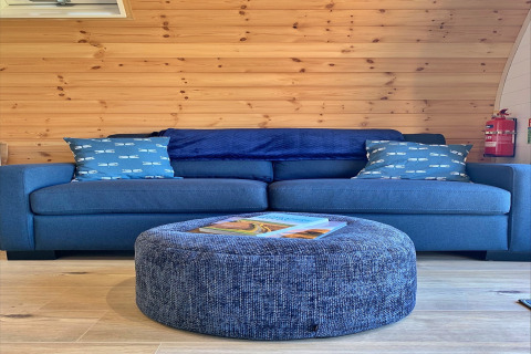 Blue sofa with patterned cushions and round ottoman in wood-panelled Deep Dale pod, United Kingdom.