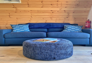 Blue sofa with patterned cushions and round ottoman in wood-panelled Deep Dale pod, United Kingdom.