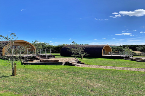 Two modern glamping pods at Deep Dale, UK, set on lush green grass under a bright blue sky.