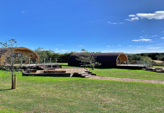 Two modern glamping pods at Deep Dale, UK, set on lush green grass under a bright blue sky.
