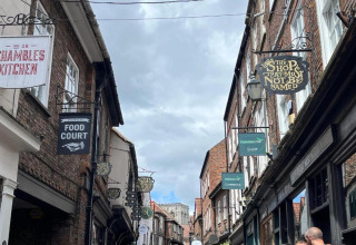 A vibrant street in the UK lined with historic brick buildings and shop signs like The Shop That Must Not Be Named.