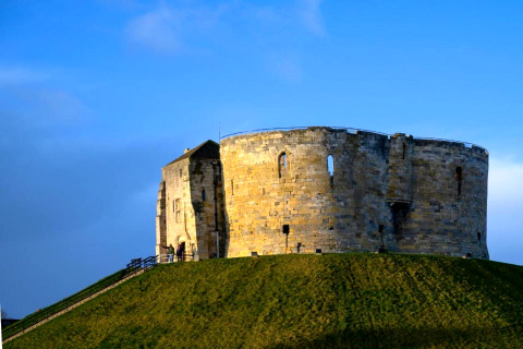 Torre di pietra rotonda su una collina erbosa con cielo blu luminoso, edificio storico ben visibile.